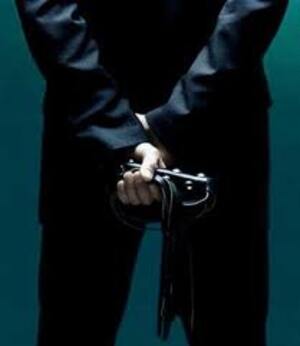 Homme en costume noir qui tient une lanière en cuir de manière explicite
